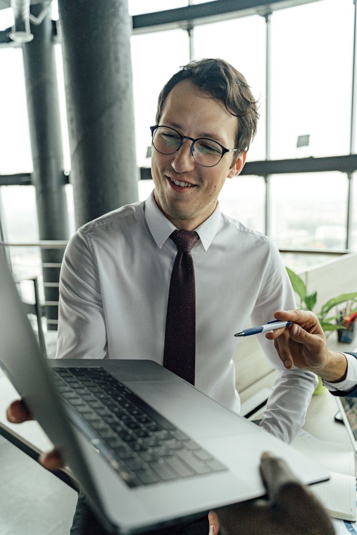 A businessman with glasses engaged in a meeting using a laptop in a modern office.