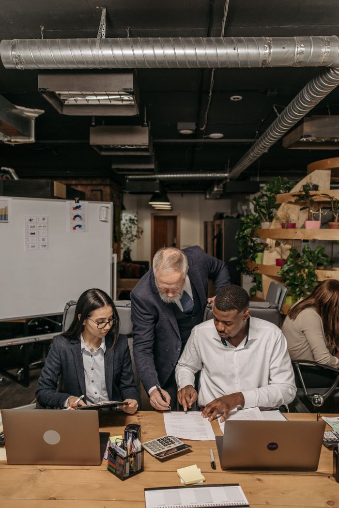 Services A diverse team collaborating at a table with laptops and documents in a modern office environment.