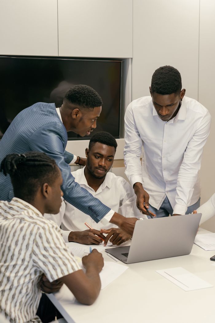 Services Four men collaborate on a project using a laptop in a modern office environment.